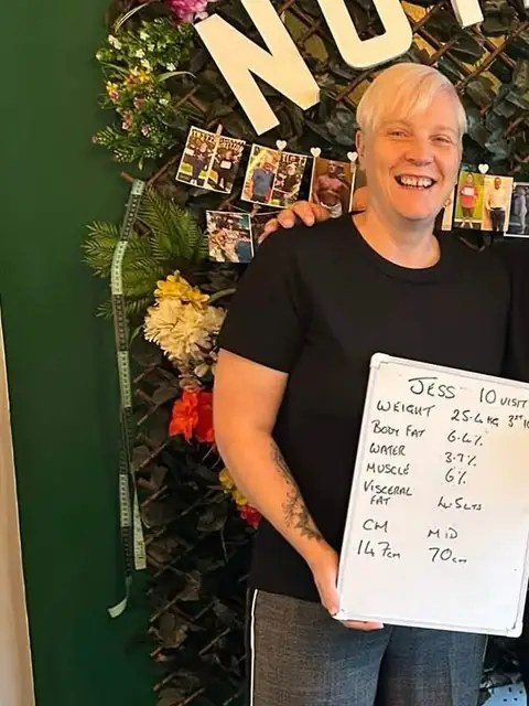 A member beams at the club, holding up what is written on her board