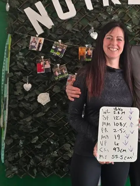 A member beams at the club, holding up what is written on her board