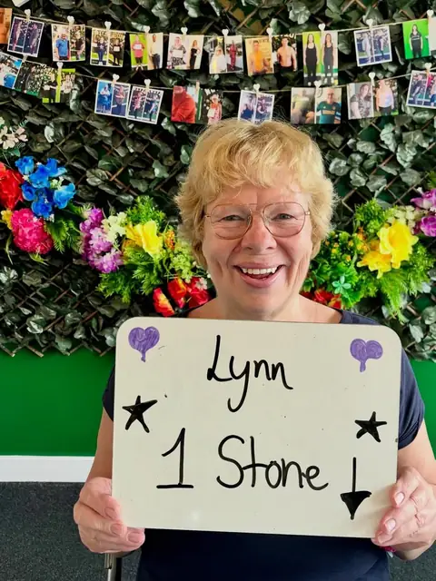A member beams at the club, holding up what is written on her board